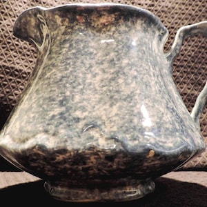 May include: A blue and white speckled ceramic pitcher with a handle. The pitcher has a rounded body and a flared lip.