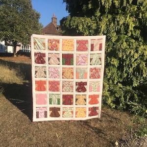 May include: A patchwork quilt made from a variety of fabrics. The quilt is made up of squares, each with a different pattern. The quilt is in shades of pink, red, yellow, and brown.