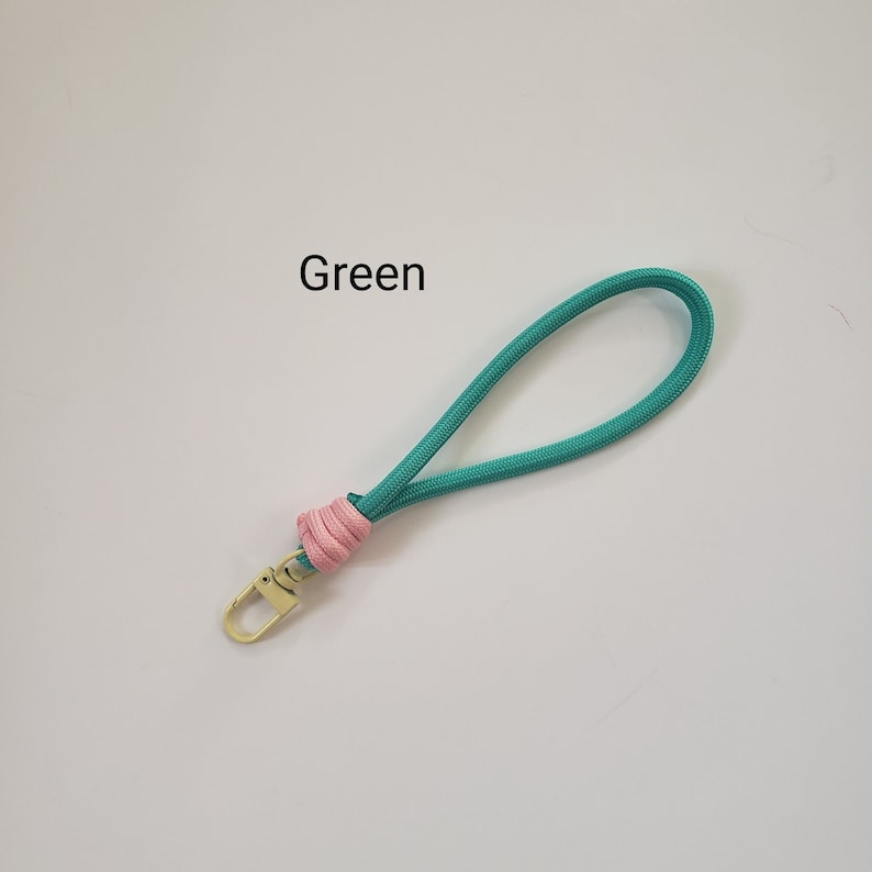 K&ouml;nnte beinhalten: Gr&uuml;ner Schl&uuml;sselanh&auml;nger mit einem rosa Knoten und einem goldenen Metallverschluss. Der Text "Green" steht &uuml;ber dem Schl&uuml;sselanh&auml;nger.