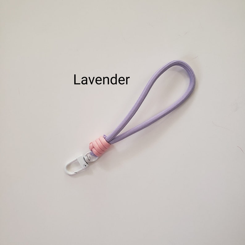 K&ouml;nnte beinhalten: Ein Lavendel-Telefonband mit einem rosa Knoten und einem wei&szlig;en Metallclip. Das Band tr&auml;gt den Schriftzug "Lavender" in schwarzer Schrift.