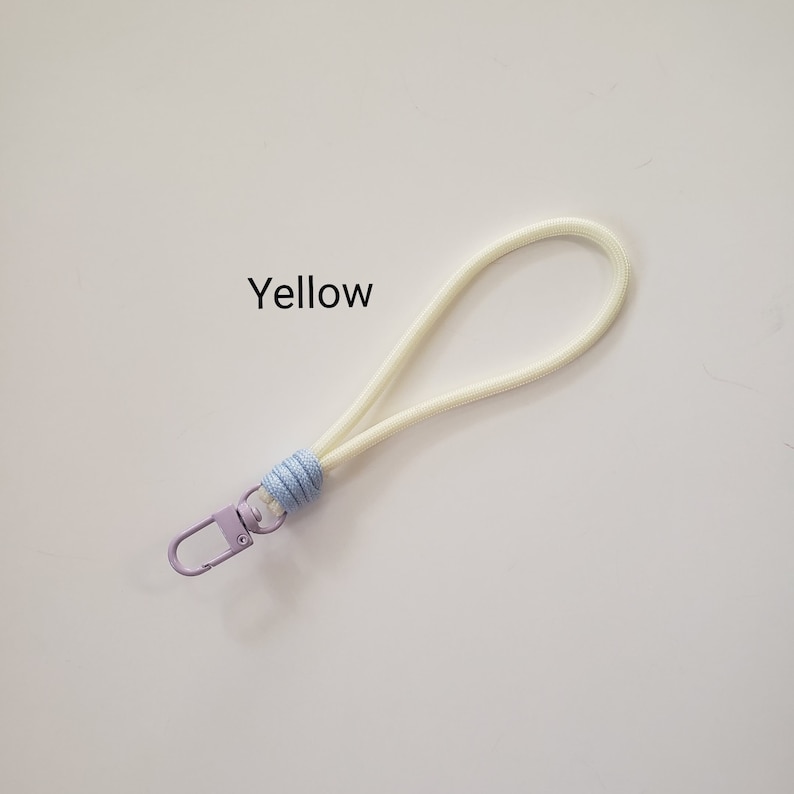 K&ouml;nnte beinhalten: Ein wei&szlig;es Lanyard mit einem hellblauen und violetten Knoten und einem violetten Metallclip. Der Text "Yellow" ist auf wei&szlig;em Hintergrund geschrieben.