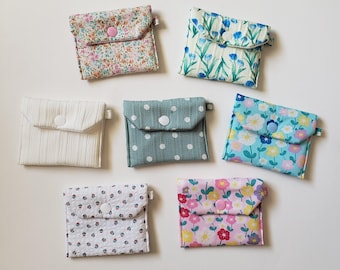 May include: Six small fabric pouches with different floral patterns and a white button closure. The pouches are arranged in two rows of three on a white surface.