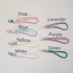 K&ouml;nnte beinhalten: Sieben bunte Schl&uuml;sselanh&auml;nger mit verschiedenen farbigen B&auml;ndern und Metallschlie&szlig;en. Die Farben sind rosa, blau, gelb, wei&szlig;, lavendel, lila und gr&uuml;n.