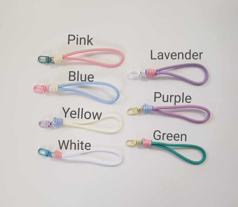 K&ouml;nnte beinhalten: Sieben bunte Schl&uuml;sselanh&auml;nger mit verschiedenen farbigen B&auml;ndern und Metallschlie&szlig;en. Die Farben sind rosa, blau, gelb, wei&szlig;, lavendel, lila und gr&uuml;n.