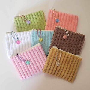 May include: Eight colorful zippered pouches with a smiley face charm attached to each zipper. The pouches are made of a soft, textured fabric and come in a variety of colors, including pink, blue, green, brown, and yellow.