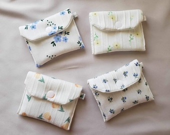 May include: Four small white fabric pouches with different floral patterns. Each pouch has a white button closure and a flap.