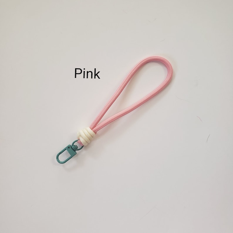 K&ouml;nnte beinhalten: Rosa Handy-Schlaufe mit einem wei&szlig;en und cremefarbenen Akzent und einem t&uuml;rkisfarbenen Metallverschluss.