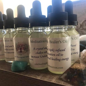May include: A row of small glass bottles with dropper tops, filled with a clear liquid. The bottles have labels with text that reads "Meditation & Healer's Oil", "A crystal and Reiki infused chakra activation oil to increase Universal healing energy", "reikihealindintuition.com", and "'s Oil".