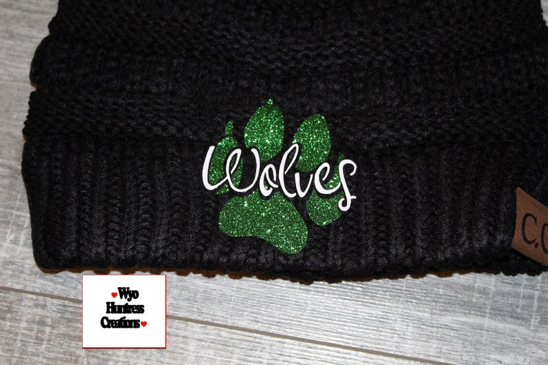 May include: Black knit beanie with a green glitter paw print and the word "Wolves" in white cursive lettering.