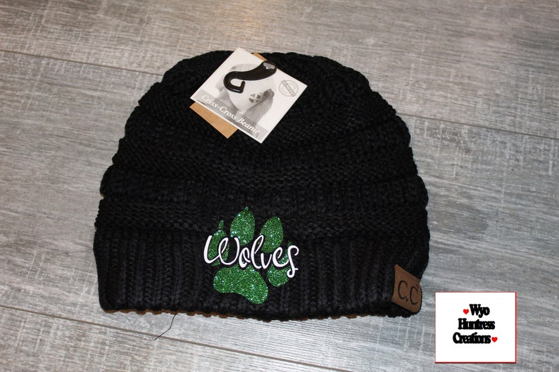 May include: Black knit beanie with a green glitter paw print and the word "Wolves" in white. The beanie has a brown leather patch with the letters "CC" on it.