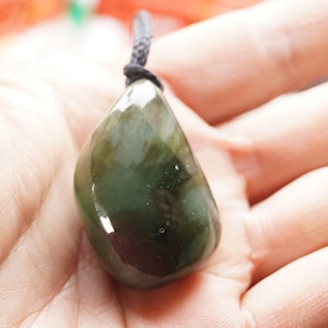 May include: A dark green, teardrop-shaped pendant made of polished stone, hanging from a black cord.