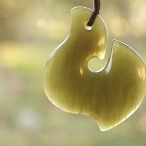 May include: A green jade pendant shaped like a fish hook, a traditional Maori symbol of good luck and prosperity.