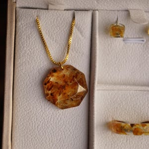 May include: A jewelry set featuring a gold chain necklace with a pendant, earrings, and a ring. The pendant, earrings, and ring have a brown and amber color. The jewelry is displayed in a white jewelry box.