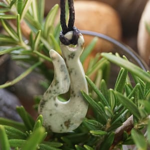 May include: A white ceramic hook pendant with a green and brown speckled pattern, hanging from a black cord.