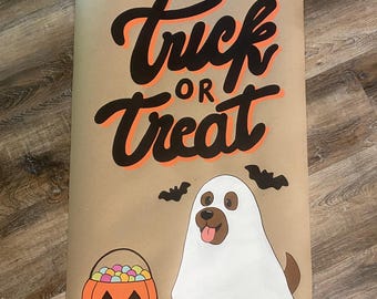 May include: A rectangular tan poster featuring the black and orange text Trick or Treat. Below the text is a brown dog wearing a white ghost costume with two black bats above it and an orange jack-o'-lantern bucket filled with colorful candies.