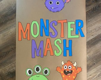 May include: A rectangular brown paper poster featuring the text MONSTER MASH in colorful block letters. Above the text is a purple winged monster. Below the text are two monsters: a green three-eyed creature and an orange spotted monster.