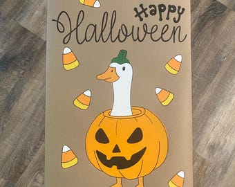 May include: A rectangular tan sign featuring the text "Happy Halloween" in black script and print. The illustration depicts a white goose with a green stem on its head, emerging from an orange jack-o'-lantern, surrounded by scattered candy corn.