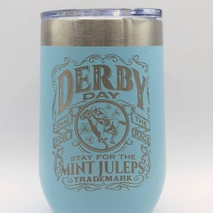 May include: A light blue stainless steel tumbler with a silver lid. The tumbler has a design that says "Derby Day Come For The Race Stay For The Mint Juleps Trademark".