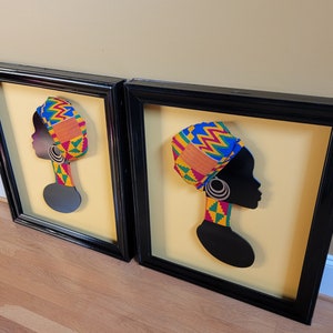 May include: Two framed black and white silhouette portraits of women with colorful patterned head wraps. The portraits are set against a yellow background.