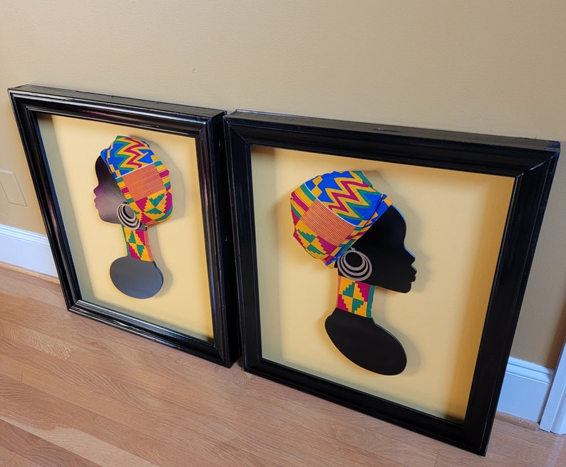 May include: Two framed black and white silhouette portraits of women with colorful patterned head wraps. The portraits are set against a yellow background.
