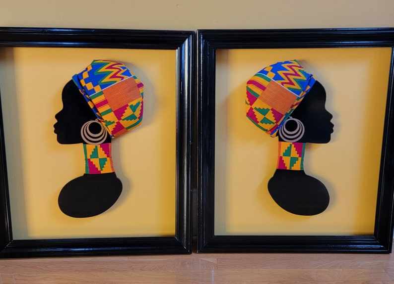 May include: Two framed pieces of art with a silhouette of a person wearing a colorful head wrap and a matching necklace. The background is a yellow color.