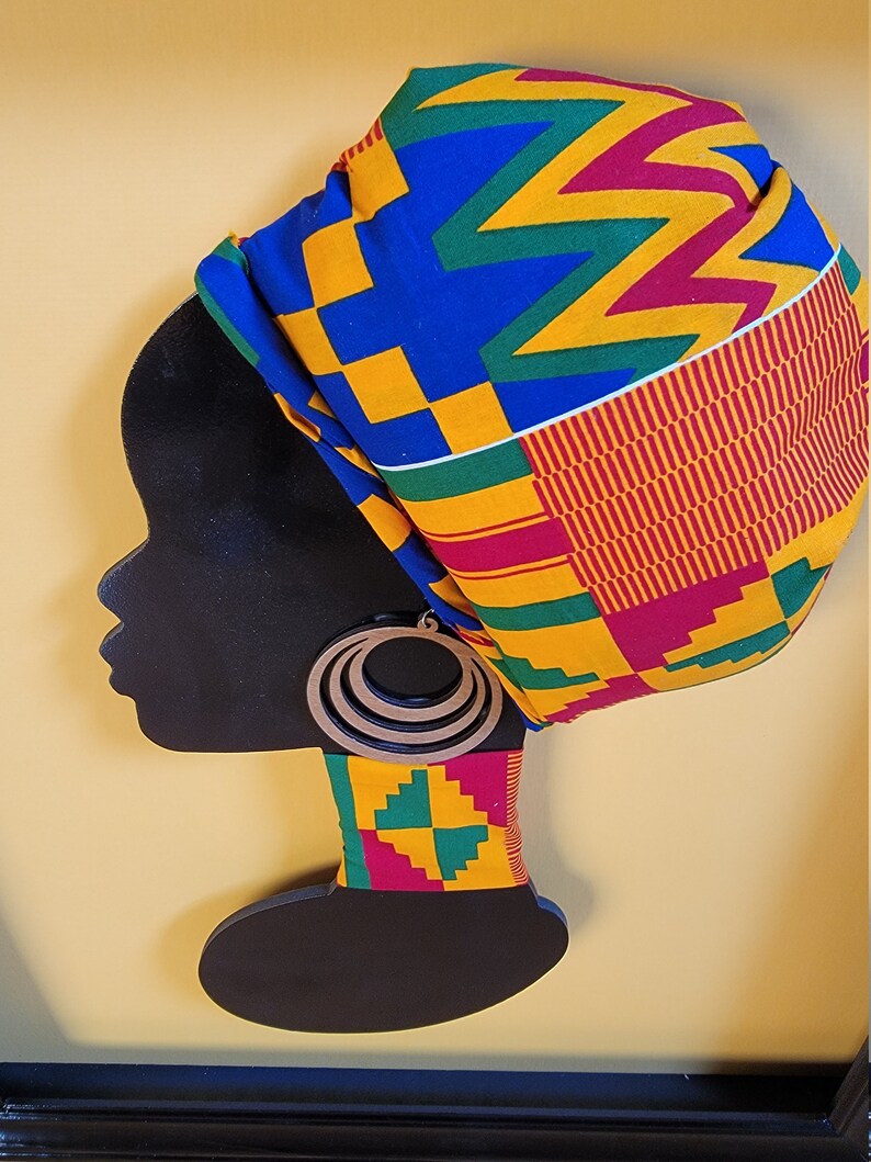 May include: A black silhouette of a woman's head with a colorful patterned fabric head wrap and large wooden earrings. The background is a yellow wall.