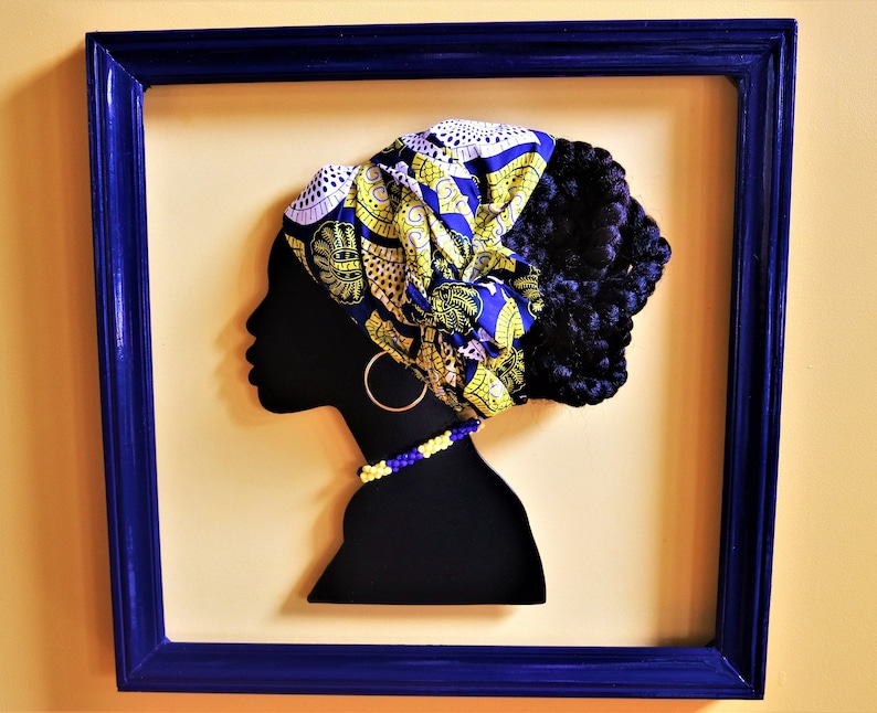 K&ouml;nnte beinhalten: Eine schwarze Silhouette eines Frauenkopfes mit einem gelben und blauen gemusterten Kopftuch, einer Perlenkette und gro&szlig;en Ohrringen. Die Silhouette ist in einem dunkelblauen Rahmen gerahmt.