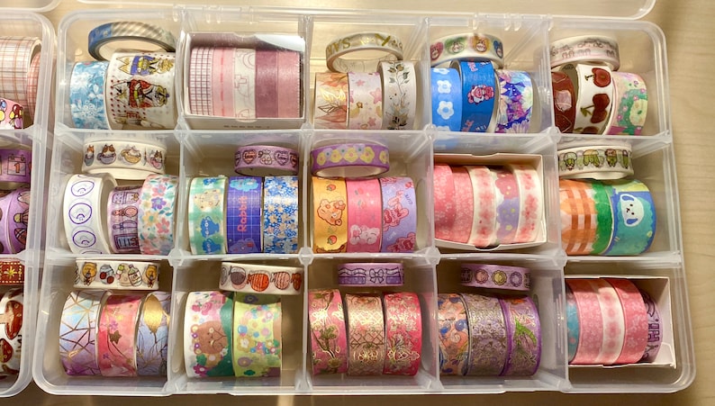 Puede incluir: Una caja de almacenamiento de pl&aacute;stico transparente llena de rollos de cinta washi de colores. La cinta washi est&aacute; organizada en filas y columnas, con cada rollo teniendo un patr&oacute;n diferente. Los patrones incluyen flores, animales, formas geom&eacute;tricas y m&aacute;s.