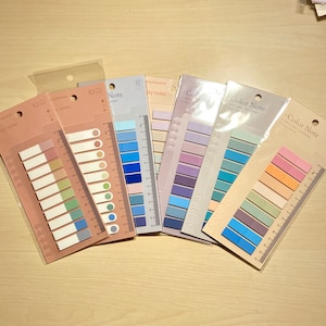 May include: A set of ten colourful sticky note pads with a ruler on the side. The pads are in various shades of blue, purple, green, and orange. The text on the pads reads "Color Note" and "Sky Notes".