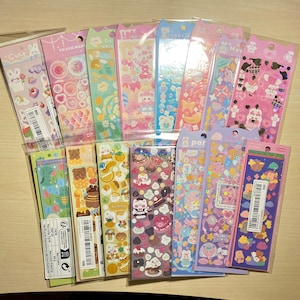 May include: A collection of 16 colourful sticker sheets featuring cute cartoon animals, food, and other designs. The stickers are packaged in clear plastic bags and are perfect for decorating planners, journals, and other items.