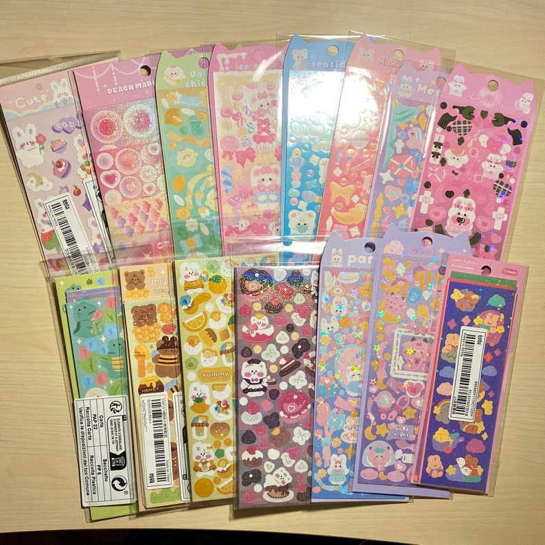 May include: A collection of 16 colourful sticker sheets featuring cute cartoon animals, food, and other designs. The stickers are packaged in clear plastic bags and are perfect for decorating planners, journals, and other items.