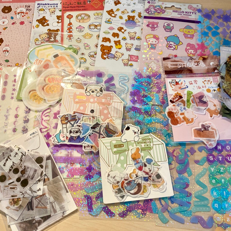 Puede incluir: Surtido de paquetes de pegatinas coloridas con varios personajes, incluyendo Hello Kitty, Rilakkuma y un gato con un lazo. Las pegatinas est&aacute;n empaquetadas en bolsas de pl&aacute;stico transparentes e incluyen dise&ntilde;os de purpurina, hologr&aacute;ficos y estampados.