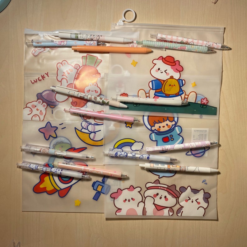 Puede incluir: Un estuche de l&aacute;pices de pl&aacute;stico transparente con cierre de cremallera. El estuche est&aacute; lleno de bol&iacute;grafos y l&aacute;pices de colores con lindos personajes de dibujos animados y dise&ntilde;os. El estuche tiene un fondo blanco con una variedad de personajes de dibujos animados, incluyendo un conejo, un oso y un gato. El texto "Lucky" est&aacute; impreso en el estuche.