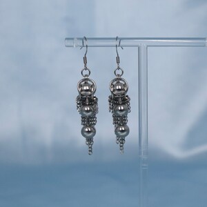 May include: A pair of silver dangle earrings with multiple small round beads and chain links.