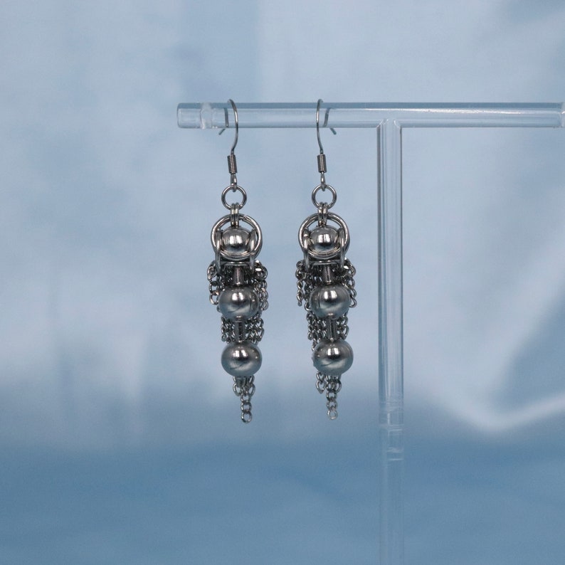 May include: A pair of silver dangle earrings with multiple small round beads and chain links.