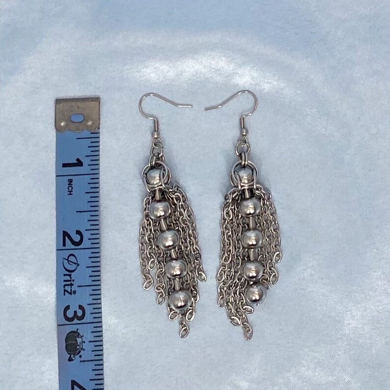 May include: A pair of silver dangle earrings with multiple chains and round beads. The earrings are approximately 5 cm long.
