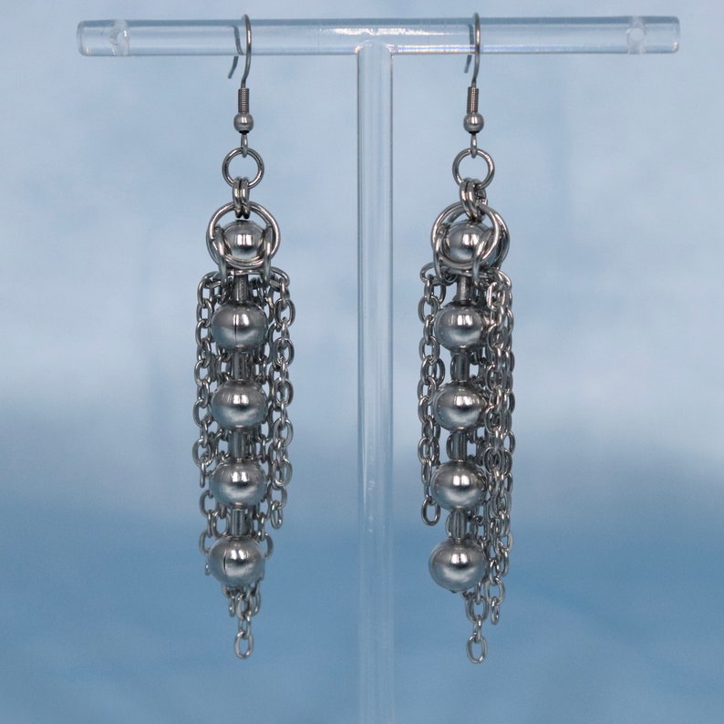 May include: A pair of silver dangle earrings with multiple chain links and round beads.