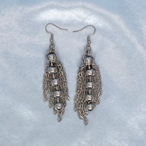 May include: Silver dangle earrings with multiple chains and round beads.