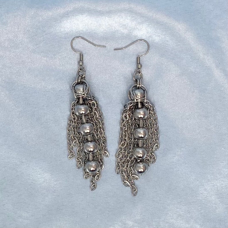 May include: Silver dangle earrings with multiple chains and round beads.