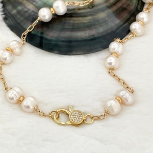 May include: A gold chain bracelet with white pearls and a sparkling clasp. The bracelet is on a white surface.