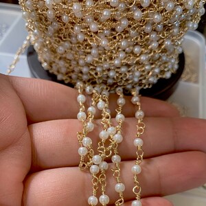 May include: A gold chain with white pearl beads. The chain is wound around a spool and a section of the chain is hanging down.