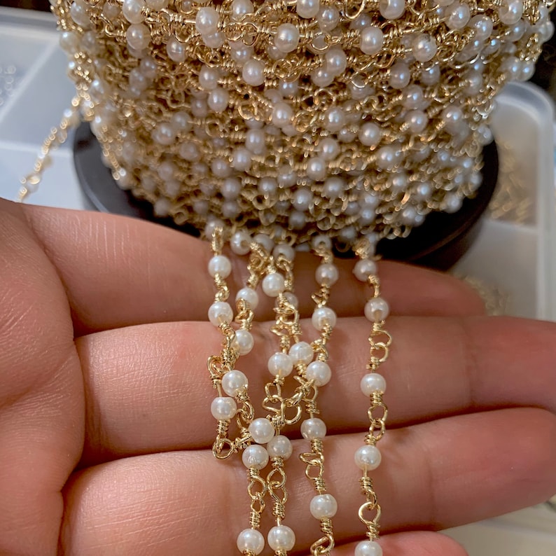 May include: A gold chain with white pearl beads. The chain is wound around a spool and a section of the chain is hanging down.