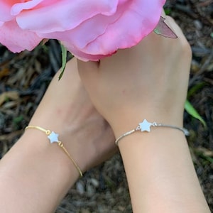 May include: Two delicate bracelets with a white star charm on each. One bracelet has a gold chain and the other has a silver chain.