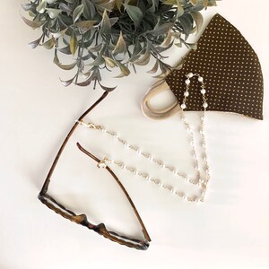 May include: A gold chain with white pearl beads, attached to a pair of glasses and a face mask. The chain can be used to keep glasses from falling off.