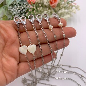 May include: Four silver chains with different styles of clasps and beads. One chain has two white heart-shaped charms.