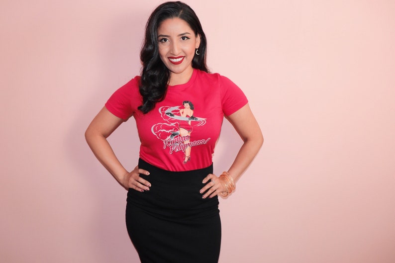 K&ouml;nnte beinhalten: Eine Frau tr&auml;gt ein rotes T-Shirt mit einem Vintage-Pin-up-Girl-Motiv und dem Text "Future Playmates". Sie tr&auml;gt auch einen schwarzen Rock und hat ihre Haare in einer Vintage-Welle gestylt.