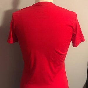 K&ouml;nnte beinhalten: Ein einfarbiges rotes T-Shirt auf einer wei&szlig;en Puppe.