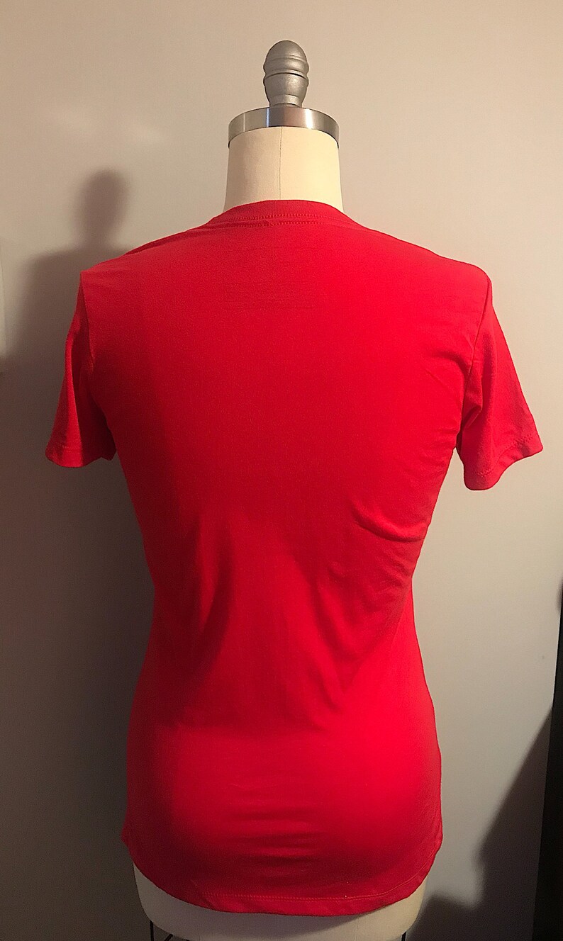 K&ouml;nnte beinhalten: Ein einfarbiges rotes T-Shirt auf einer wei&szlig;en Puppe.
