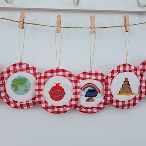 May include: Six red and white gingham fabric ornaments with different embroidered designs. The designs include a book titled "The Story", a globe, a pomegranate, a rainbow over a pot, a tower, and a hedgehog with stars.
