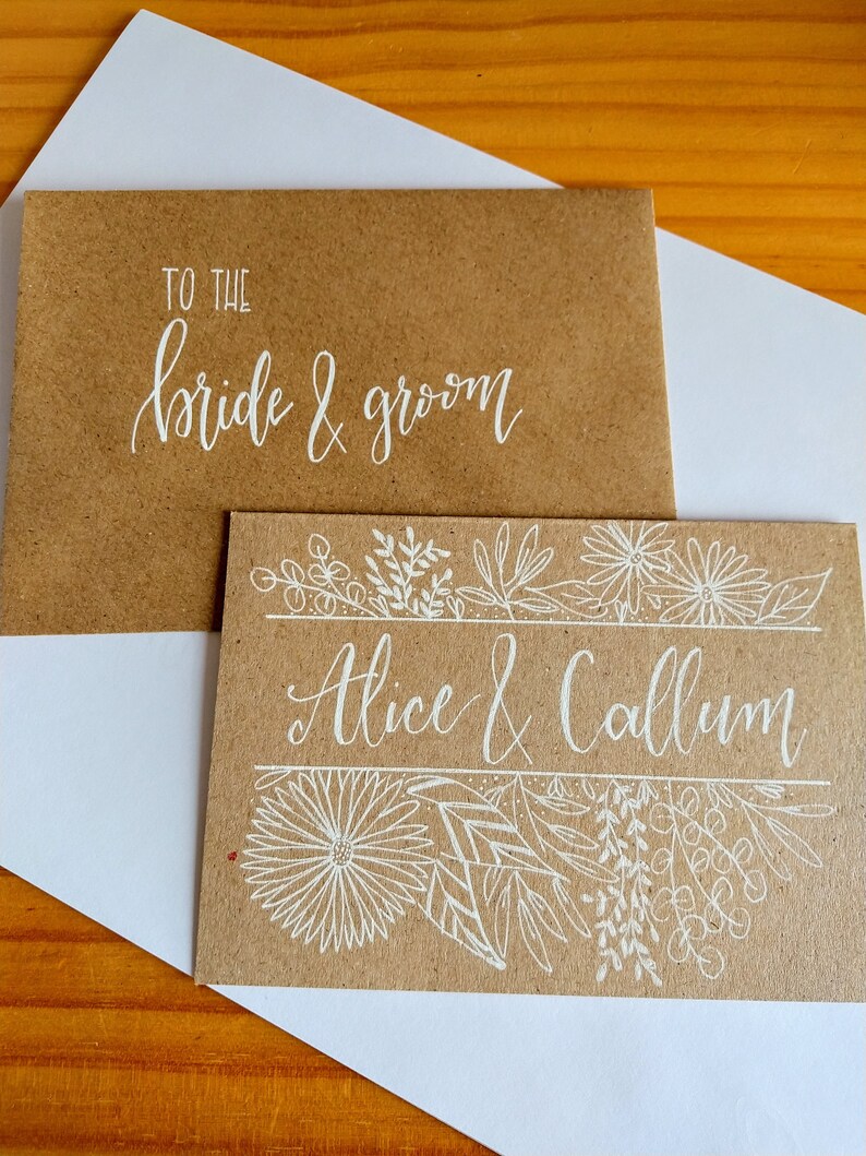 May include: A brown card with white calligraphy that reads "To the bride & groom" and a second card with white calligraphy that reads "Alice & Callum" and a floral design.